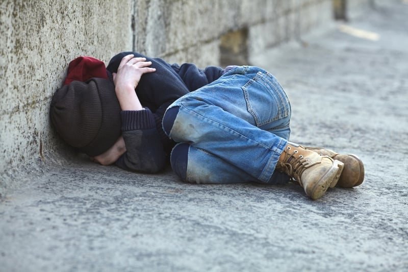 A young boy laying on the ground with his head against a wall