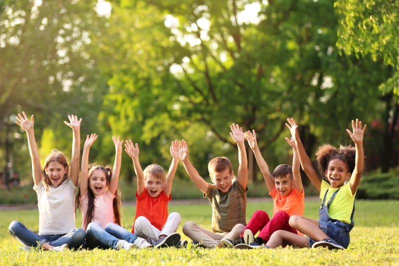 A group of children sitting on the grass with their hands in the air
