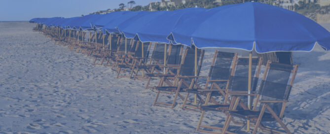 Row of blue umbrellas and wooden chairs on sandy beach