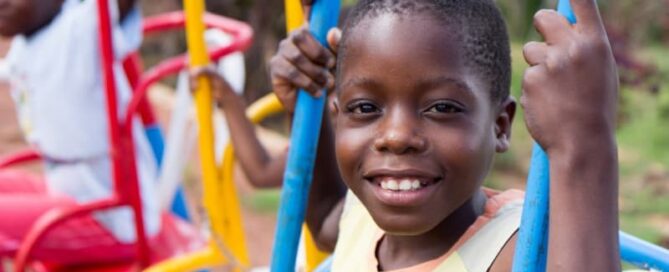A smiling 13-year old Ugandan boy swinging on a colorful swing